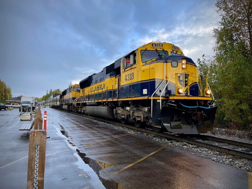 A yellow and blue passenger train rest beside a rain-soaked platform