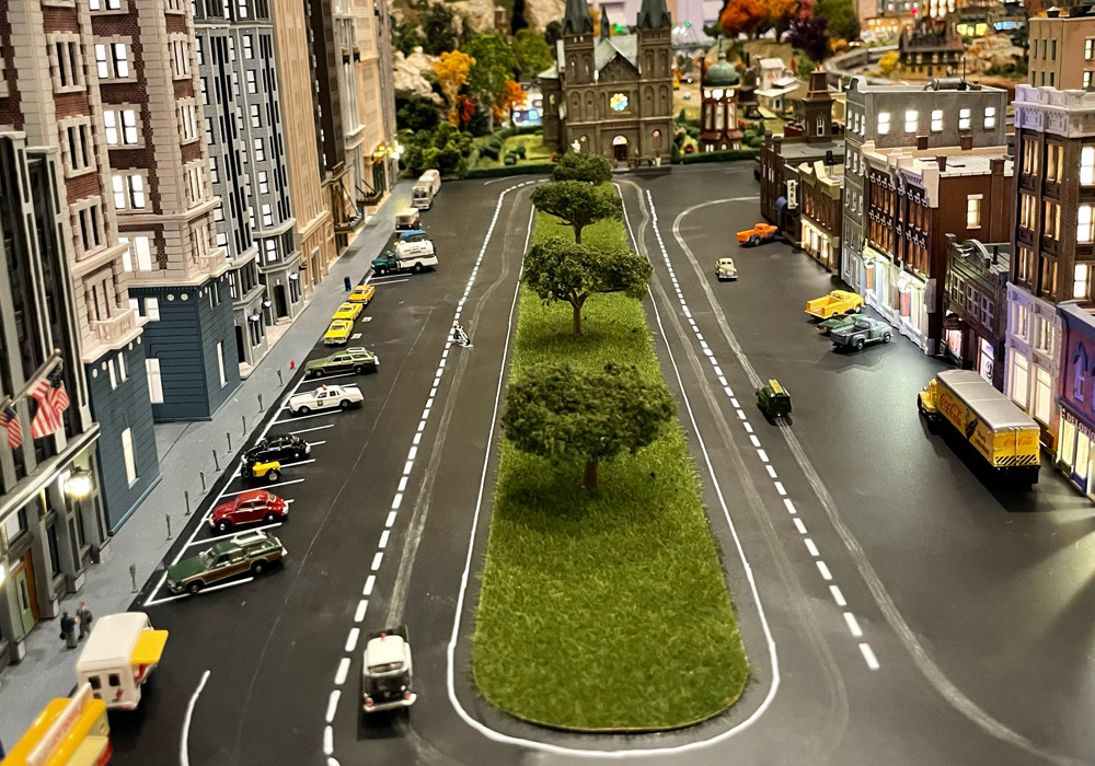 Miniature vehicles follow a track around city streets on a model railroad
