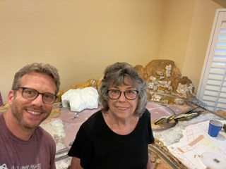 A man and woman smile in front of a partially completed train table