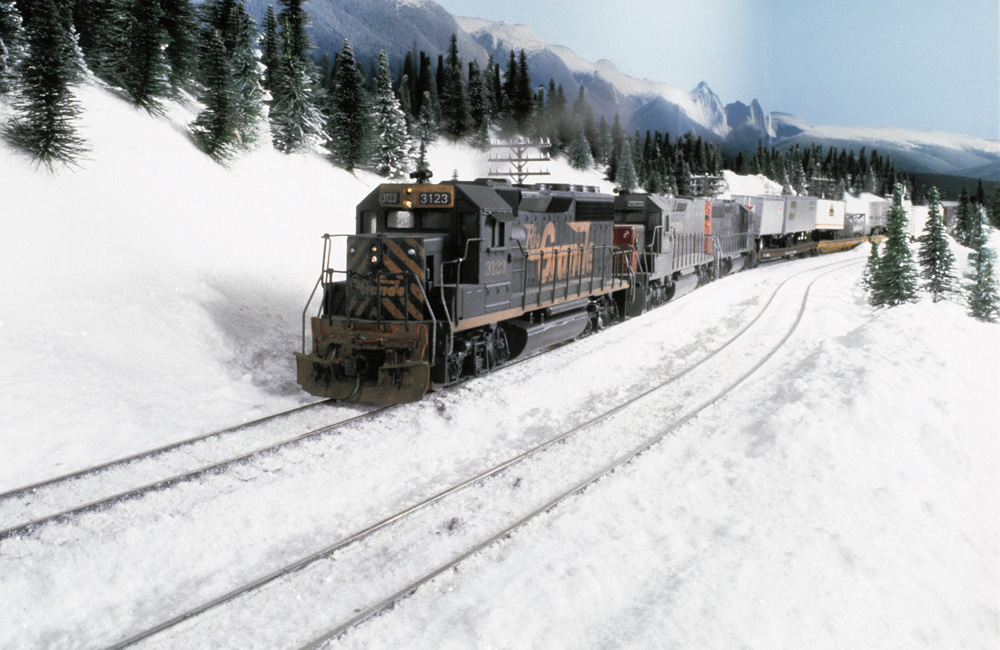 A trio of diesels pulls an intermodal freight train through a snowy mountain landscape