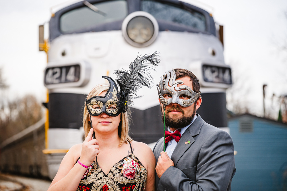 a man and woman with masquerade masks in front of silver train