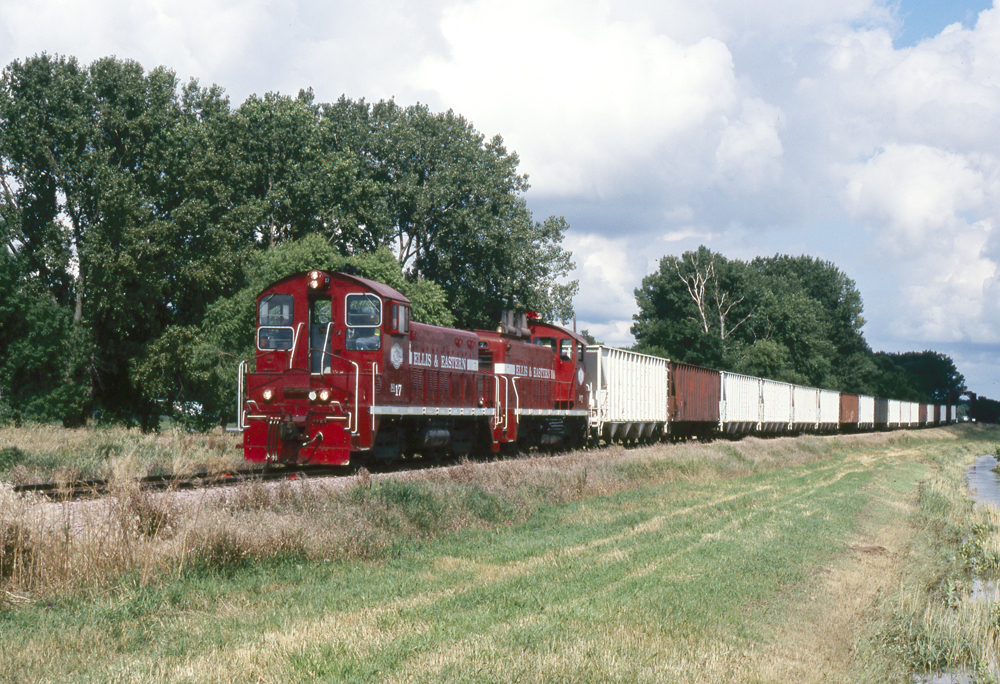 Red diesel switchers pulling a freight train of hoppers.