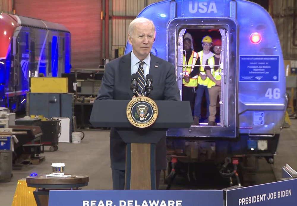 Man speaking at podium with passenger car in background