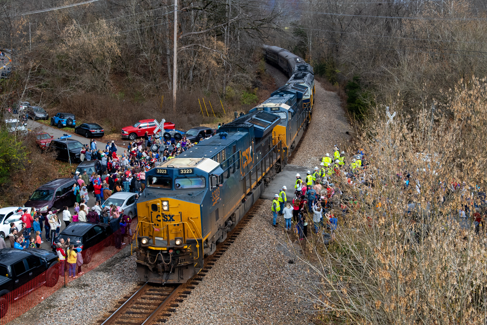 Freight locomotives lead passenger train around curve with crowd of people waiting