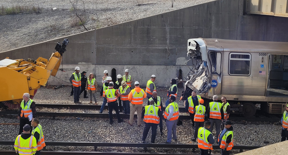 People in safety gear at site of crash between rapid-transit train and maintenance equipment