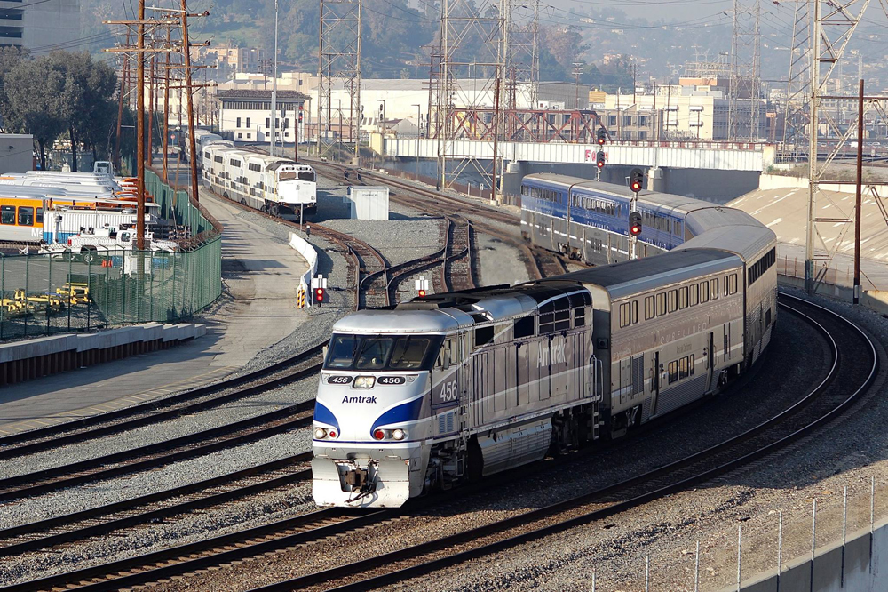 Passenger train rounds curve with tower and commuter train in background