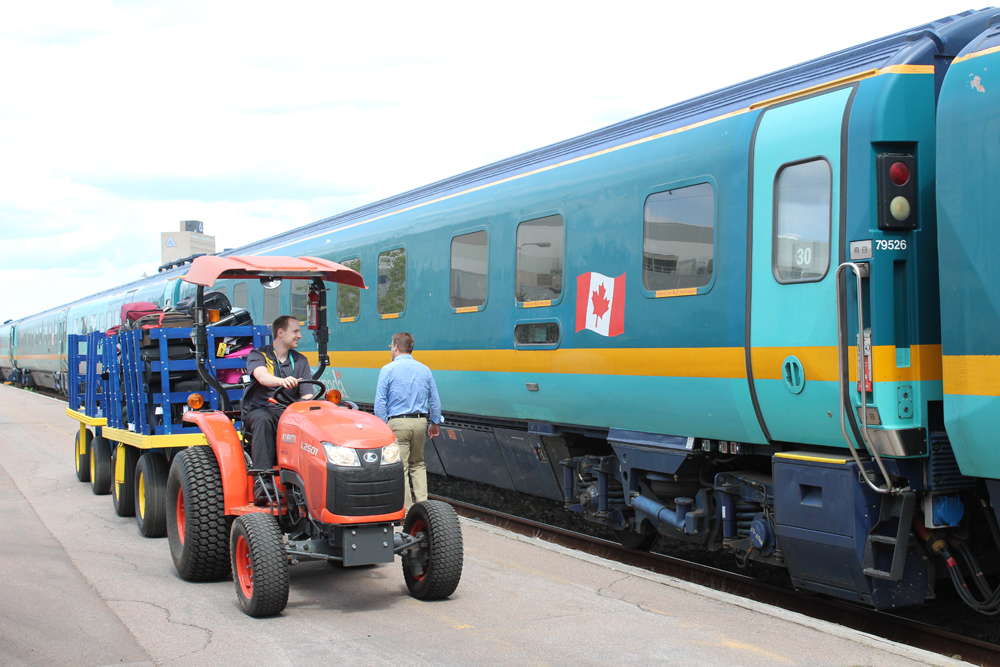 Small tractor pulling luggage cart next to passenger train