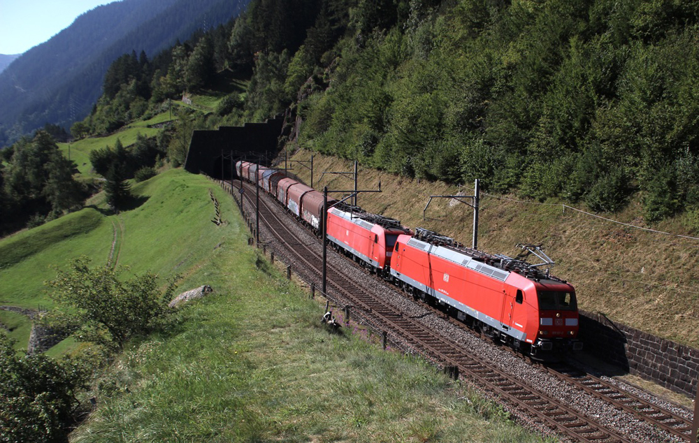 Freight train with two red electric locomotives in mountains