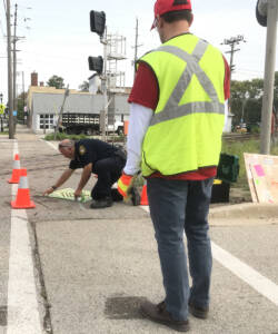 Two men spray painting a warning sign on a grade crossing.