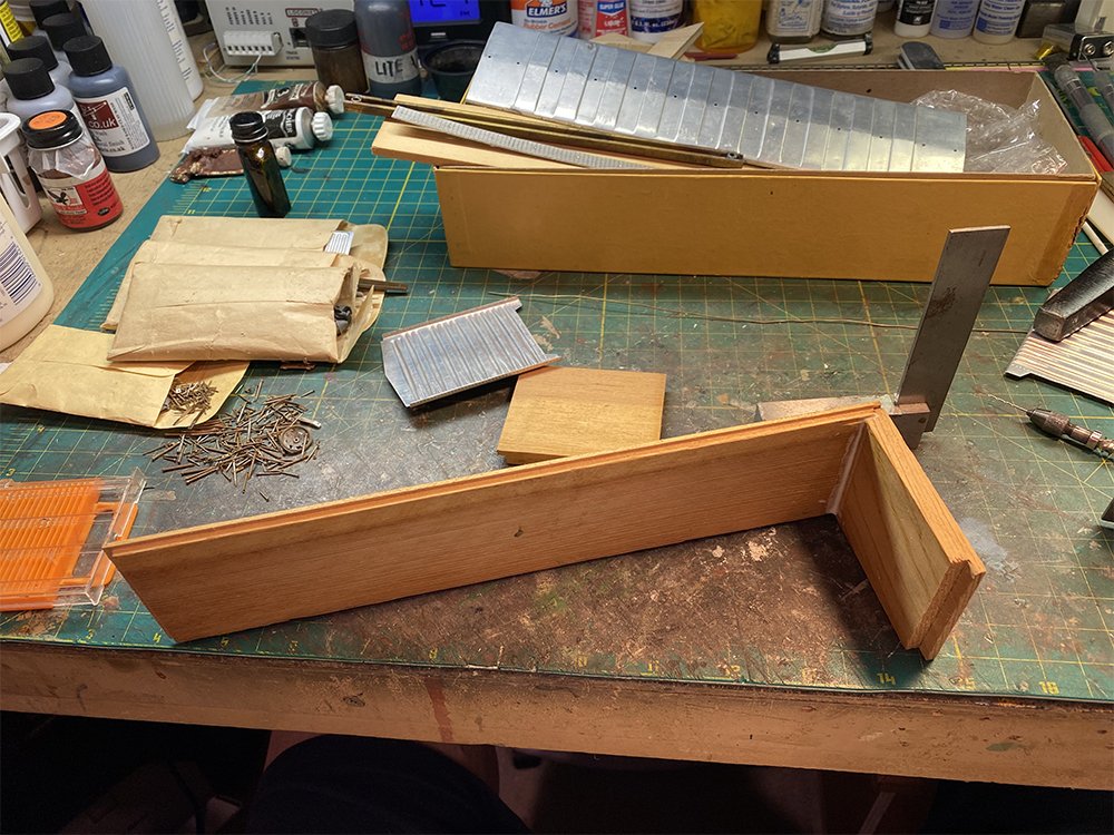 brown wood rectangular model train boxcar floor with tan wet glue on joint between brown wood rectangular end piece on green workbench top.