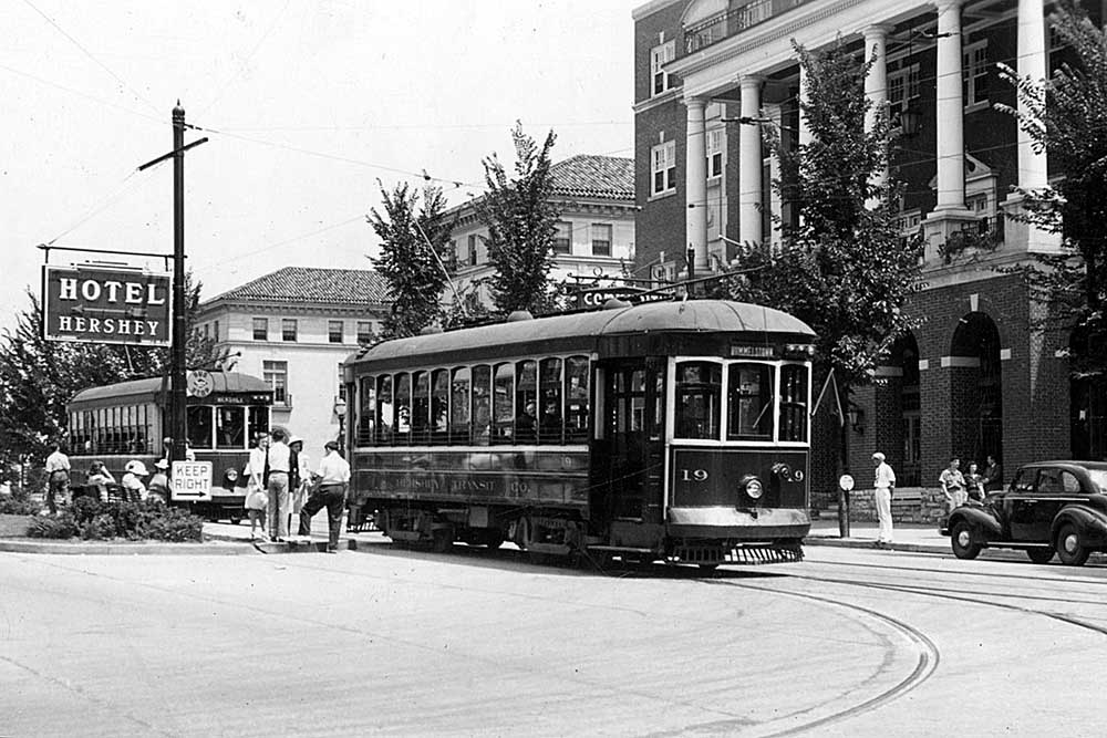 Two trolley cars parked on street in front of brick hotel