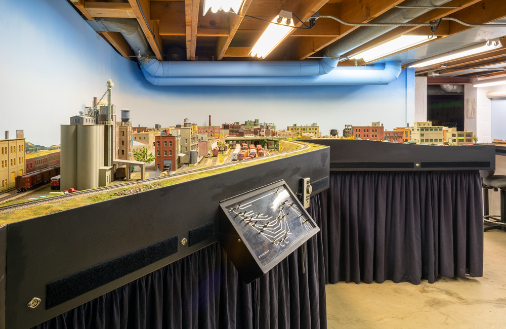A model railroad in a basement, with exposed beams and air ducts above