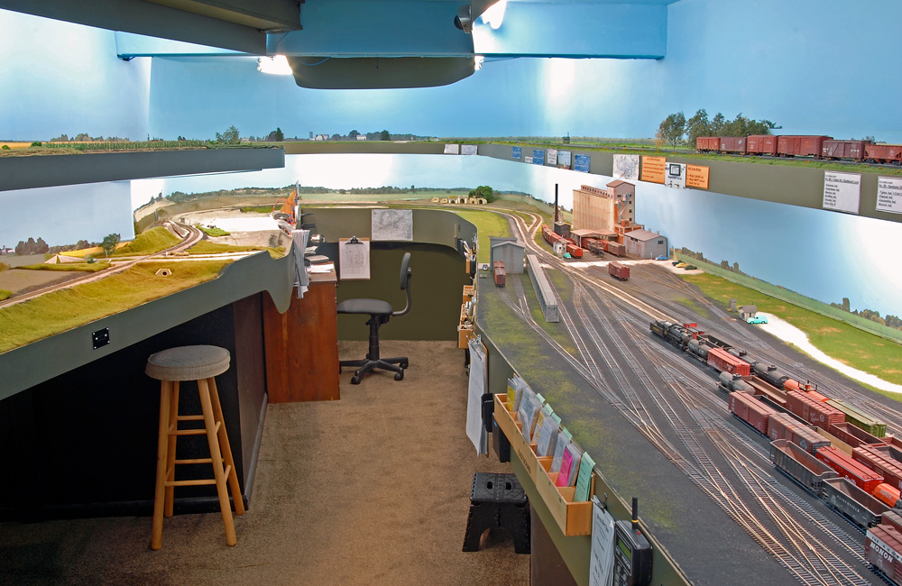 Two decks of a model railroad curve around the walls at the end of an aisle