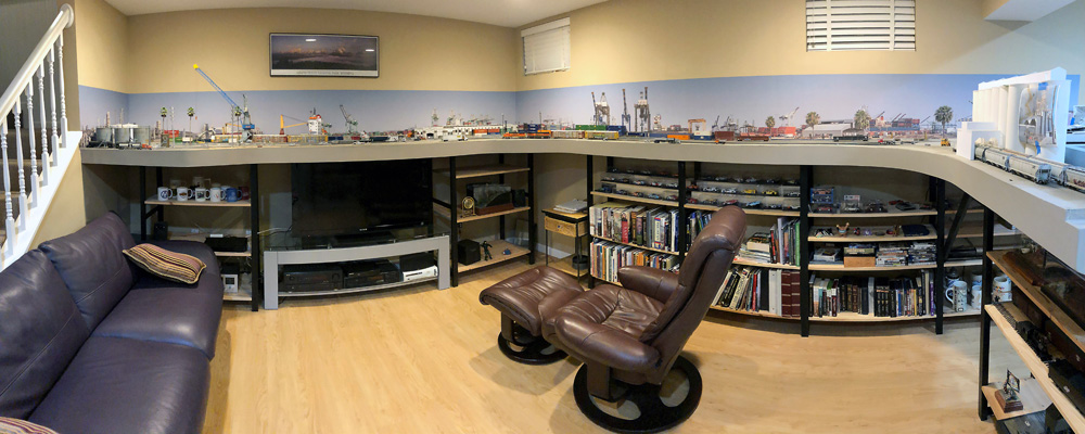 A panorama of a basement family room with a train layout built around three walls
