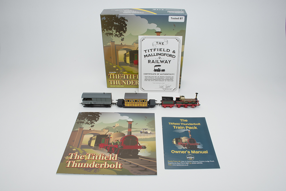 Three small toy train models, a large colorful box with a train on the cover, two booklets with blue and green covers, and a piece of tan paper.