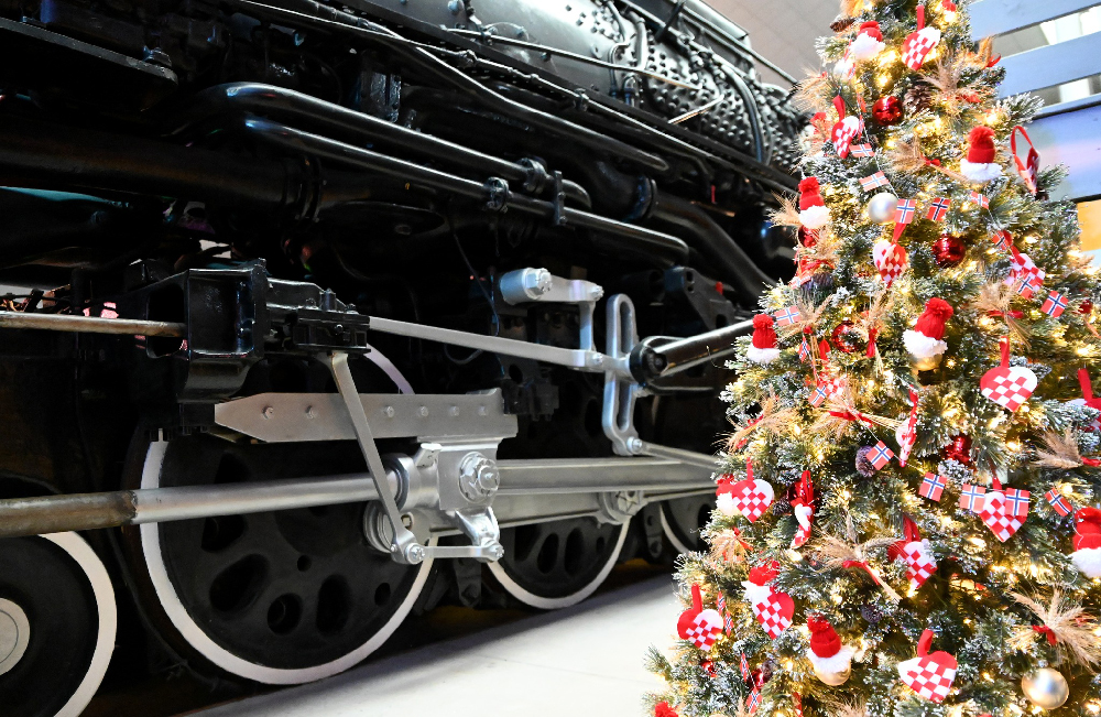 Christmas tree next too a black steam locomotive. Christmas and trains.