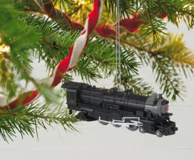 Black steam locomotive ornament hanging on the branches of a Christmas tree.