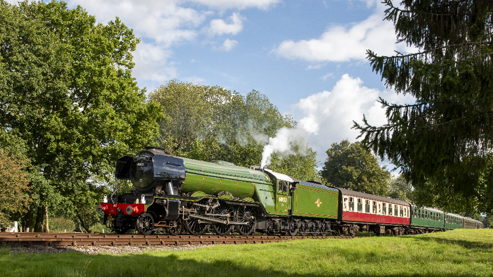 Large green British steam locomotive pulling a passenger train.