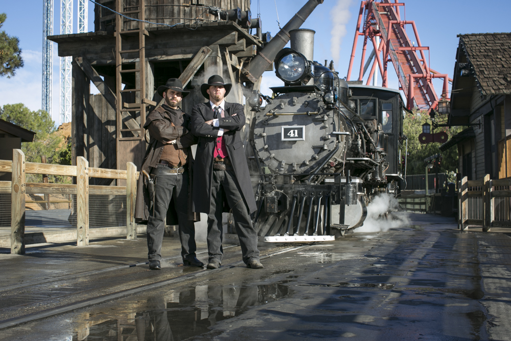 Bandits pose in front of steam locomotive at a western-style town 
