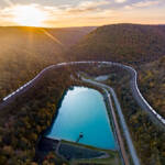 Aerial image of train traveling around fall-colored mountain.