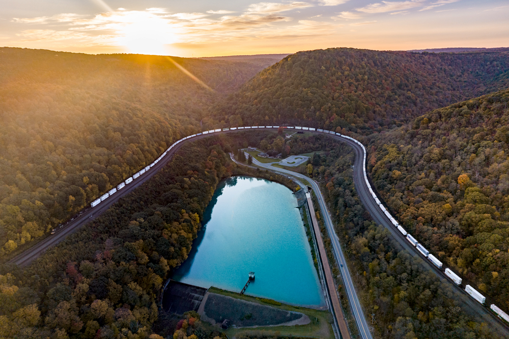 Aerial image of train traveling around fall-colored mountain.