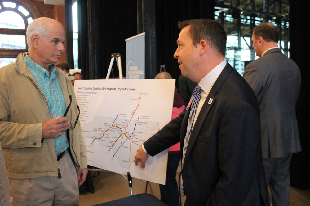 Man in suit gesturing to map of rail routes