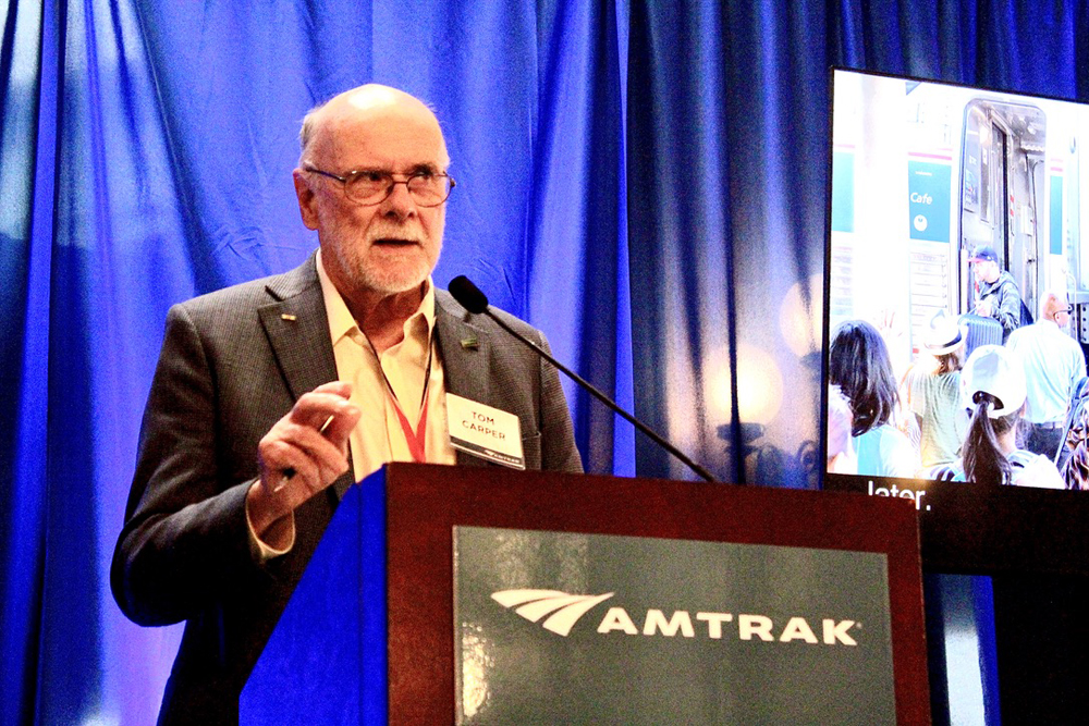 Man with beard speaking at Amtrak podium