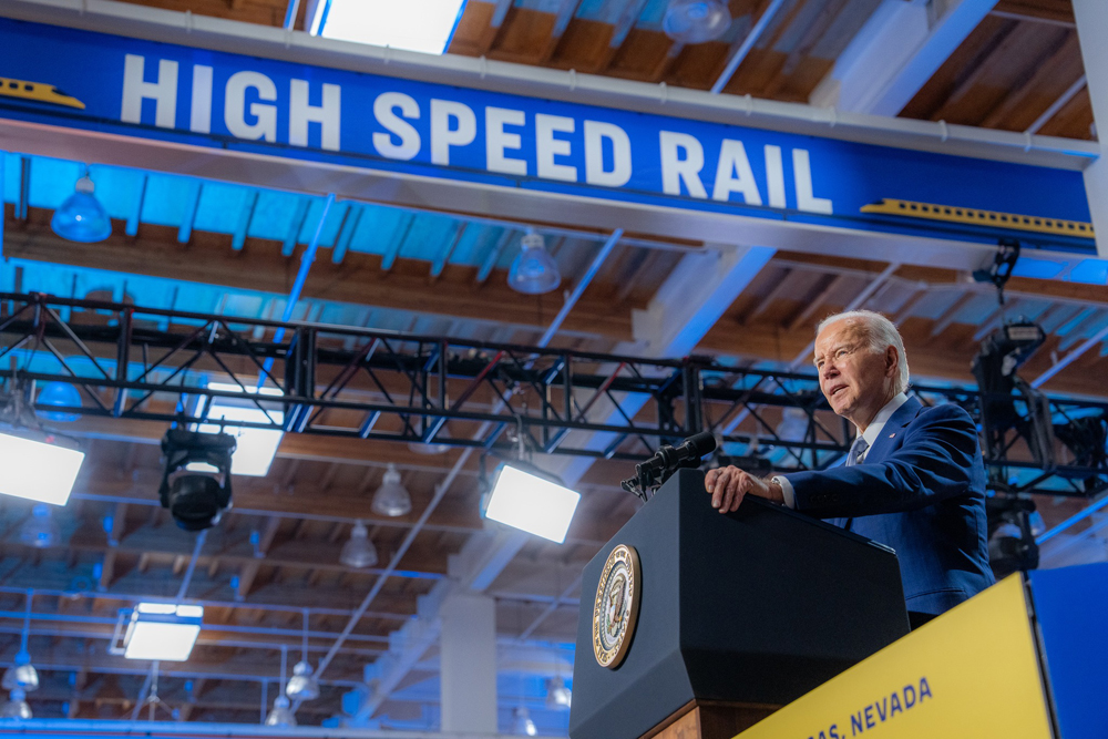 President Joe Biden speaking at podium with banner reading "high speed rail" above him