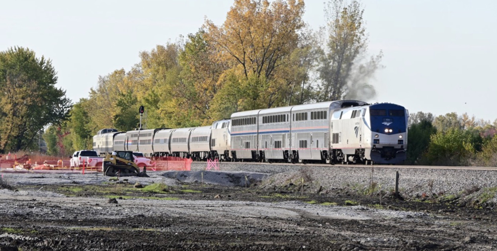 Amtrak train with locomotive and three cars, followed by another locomotive and a mix of car types