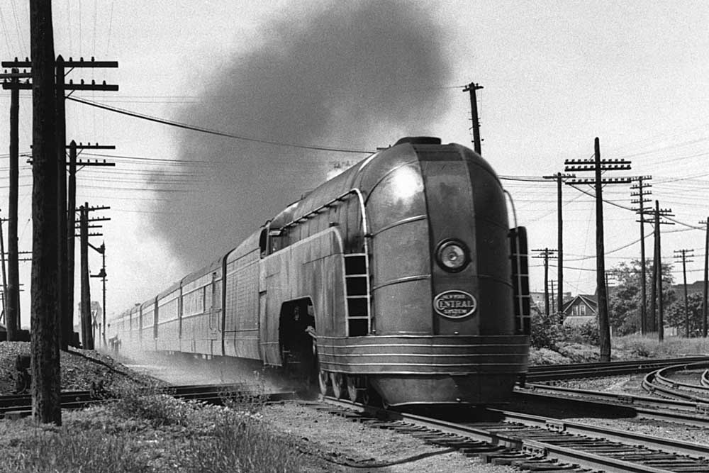 Streamlined steam locomotive on passenger train among many wires