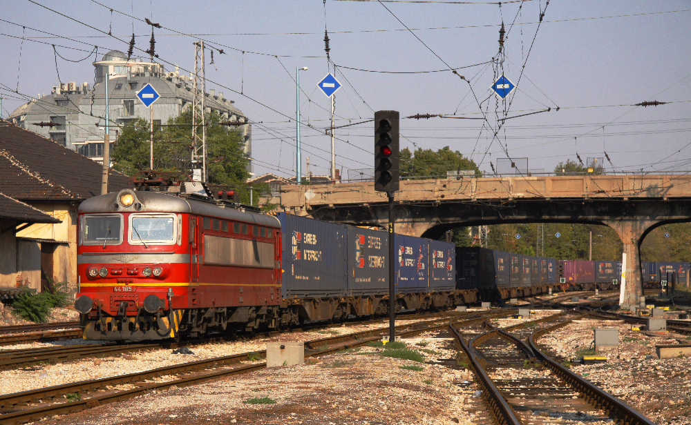 Older red European electric freight locomotive pulling a container train.