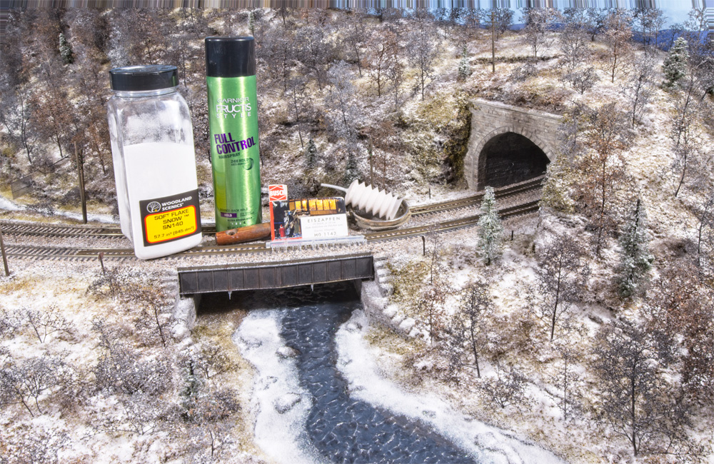 An assortment of scenery supplies sit on a bridge over a frozen creek on an HO scale model railroad
