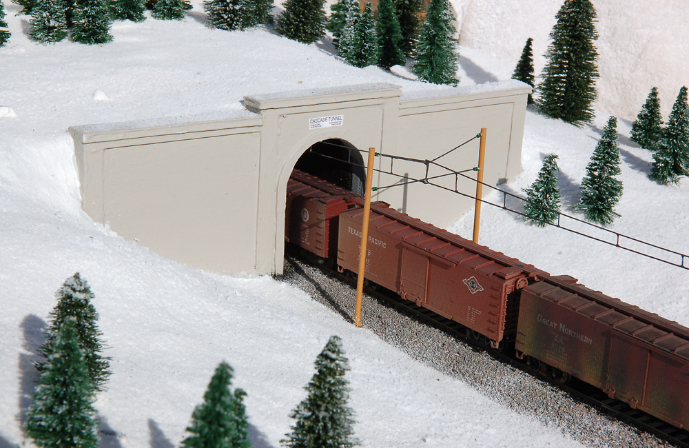 A train emerges from a tunnel under catenary in a snow-covered landscape