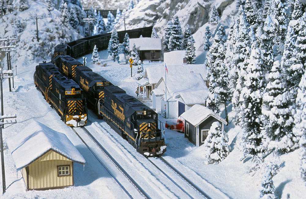 Black locomotives lead an empty coal train around a curve through a snow-covered scene