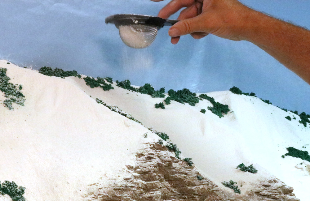 White powder is sifted onto model railroad terrain