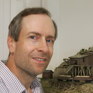 A man smiles in front of a model railroad layout