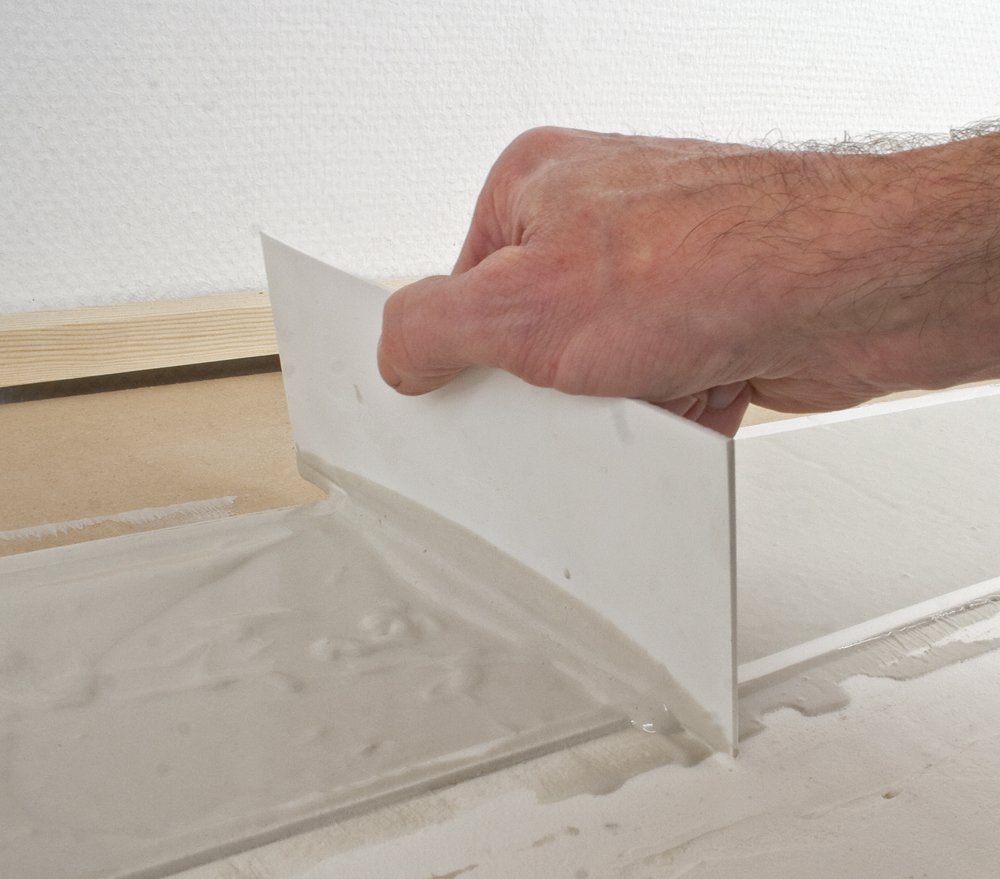 Photo of man’s hand using a piece of styrene to smooth plaster on a model railroad.