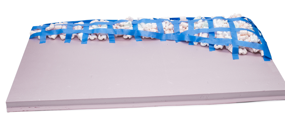Color photo of pink extruded-foam insulation board partially covered with tape and packing peanuts.