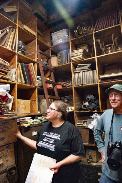 Two people in a archive with books, records, documents.