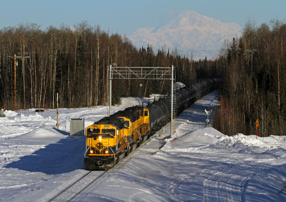 Freight train in snow with mountain in background.