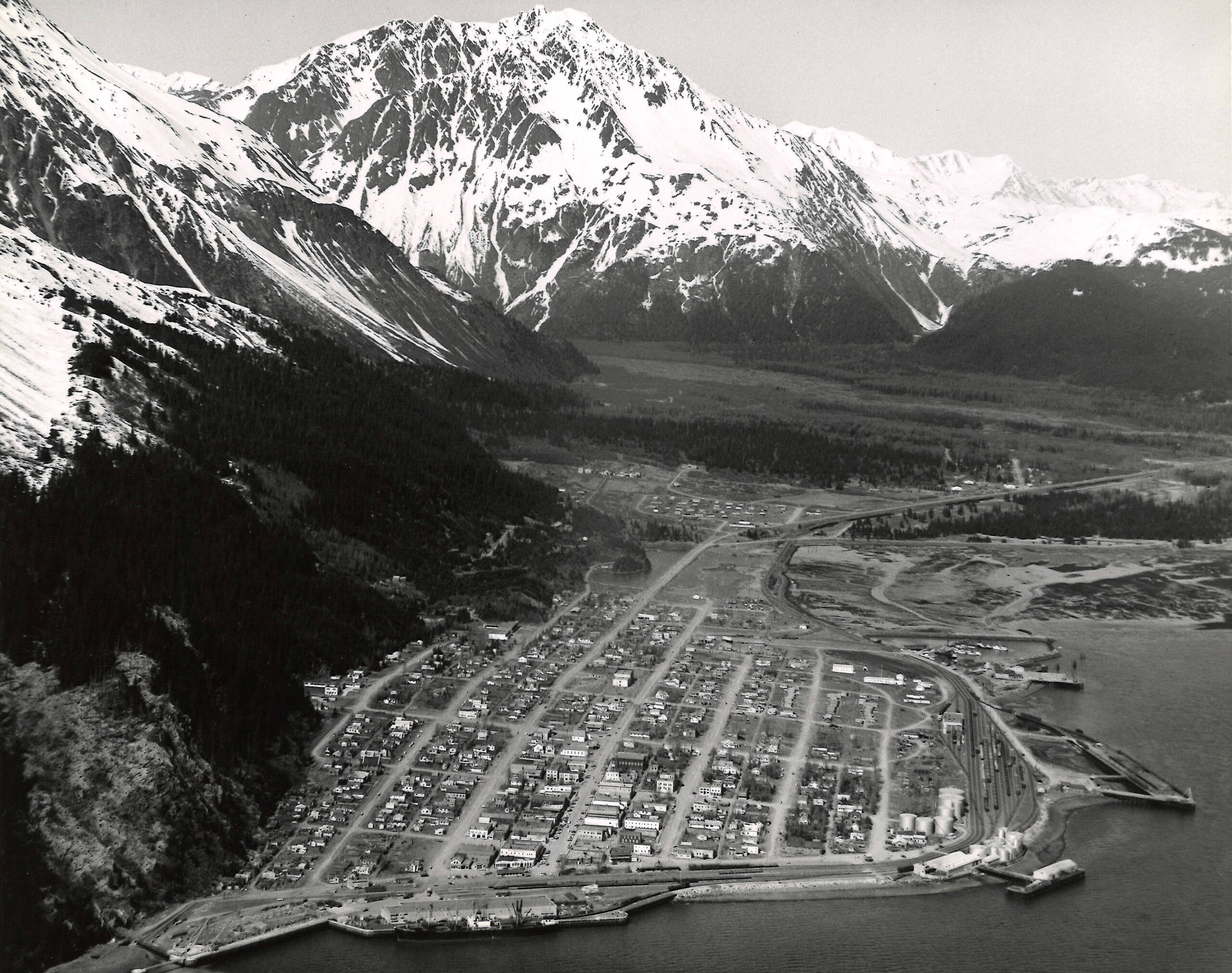 Aerial photo of city on a river with high mountains in background.