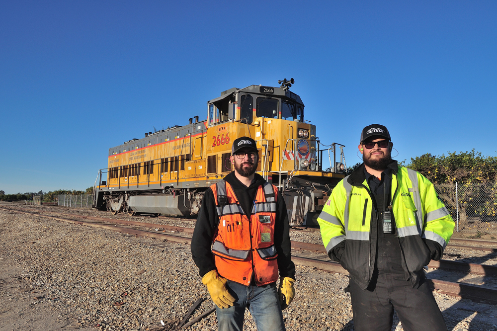 two men in front of locomotive with bright coats on