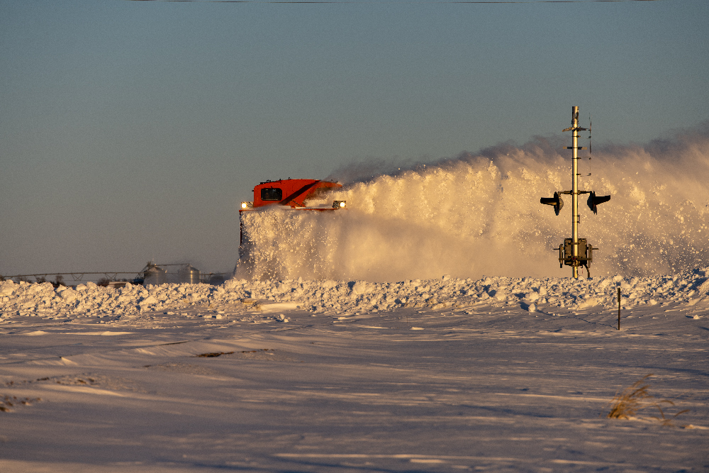 Orange rotary snow plow working through a deep drift.