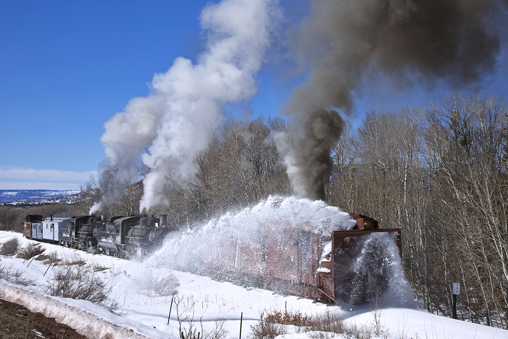 rotary snow plow on track with trees behind it