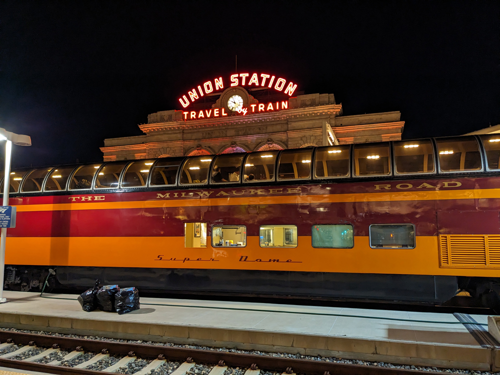 An orange passenger car with a dome sits in front of Denver’s Union Station.