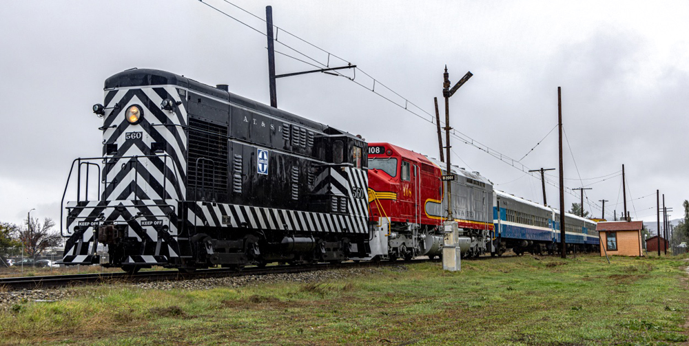 Black switcher with zebra stripes and warbonnet locomotive with passenger train