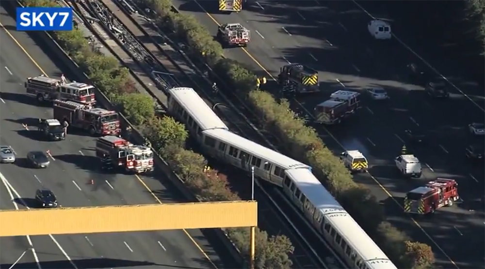 Two derailed cars of rapid-transit train in center divider of highway