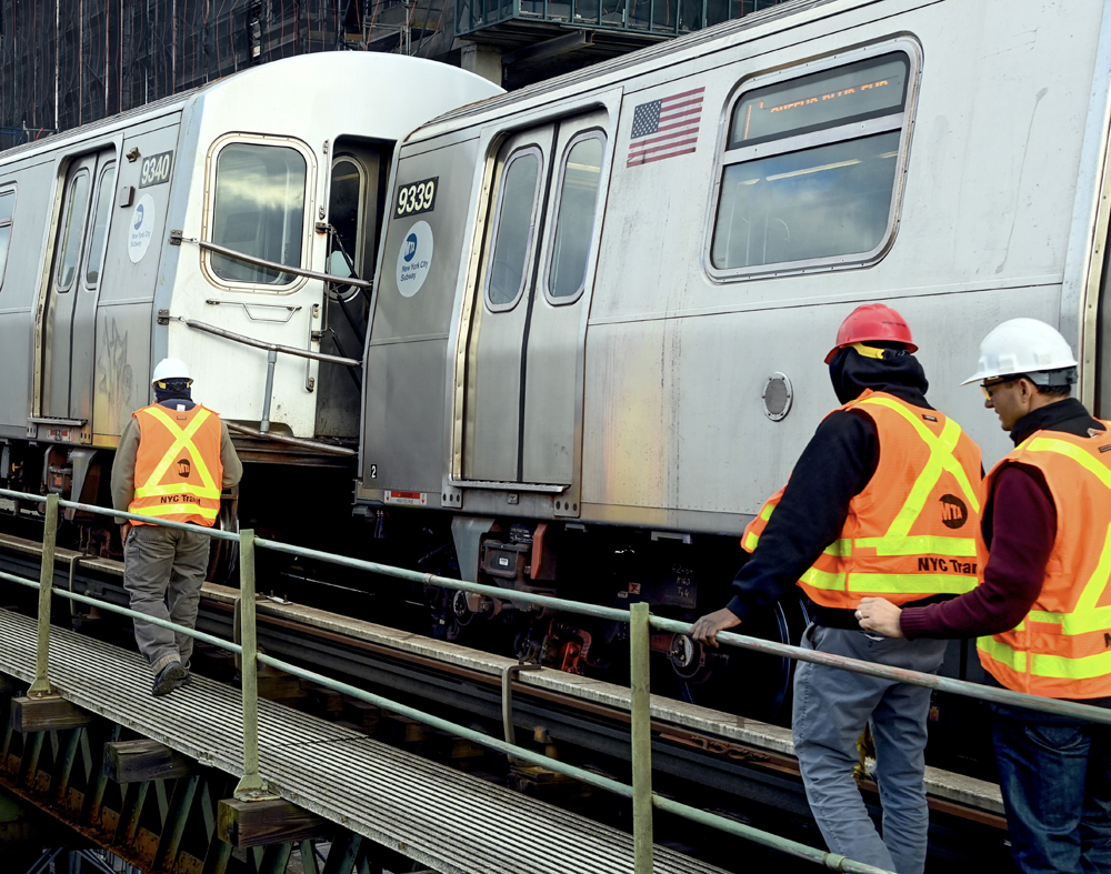 Men on walkway next to derailed subway cars