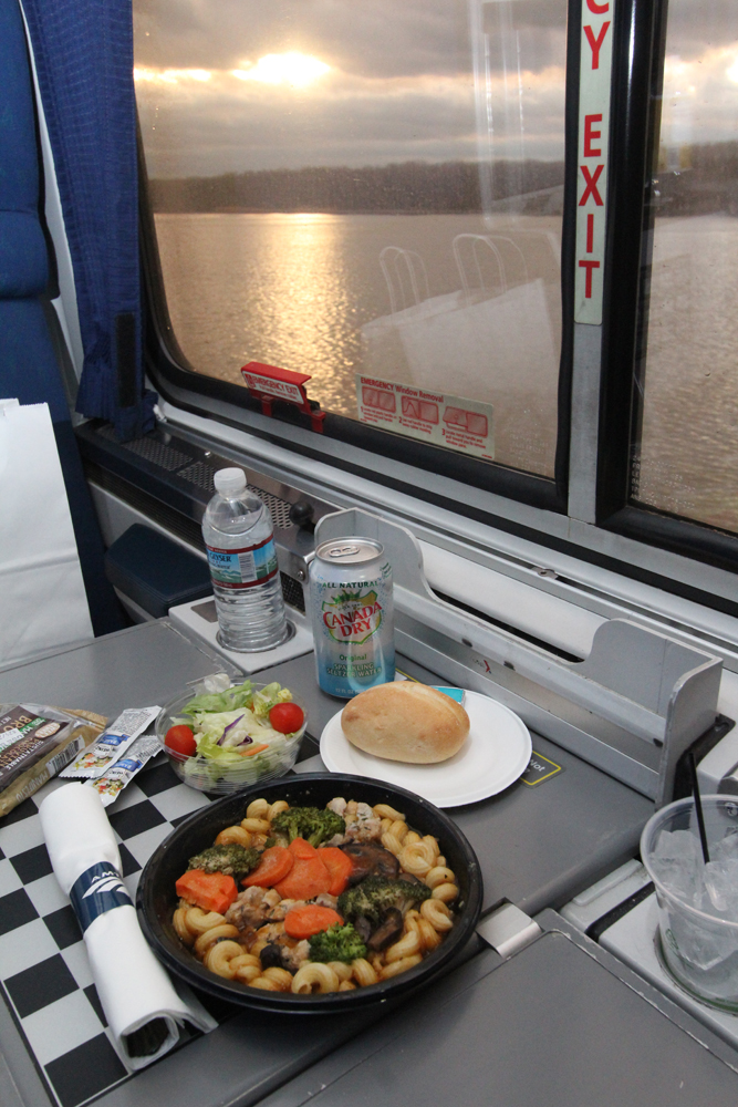 Food on table in dining car with sunset reflecting on river outside window