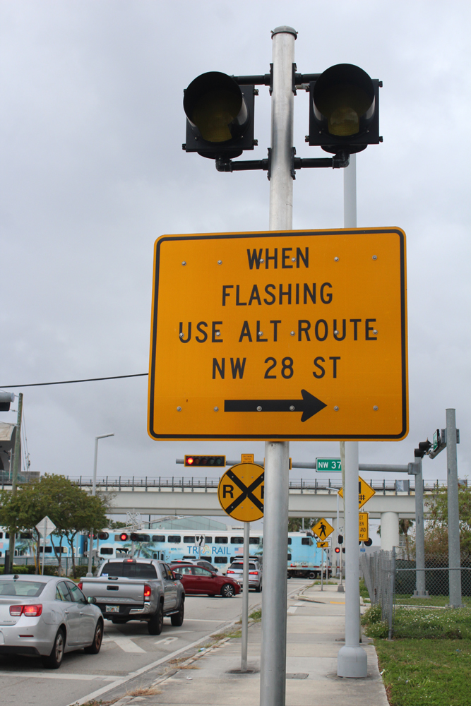 Street sign mounted below flashing lights reading, "When flashing use Alternate route, NW 28 Street"